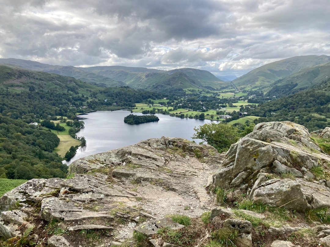 green lake surrounded by green mountains under white clouds during daytime